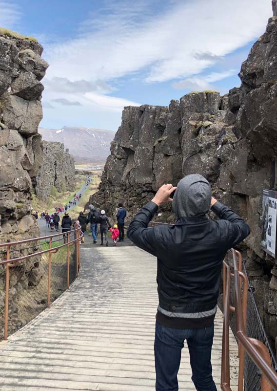 A tourist takes a photo of within a narrow rocky canyon.