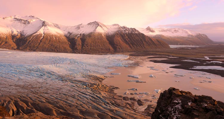 A glacier stretches below snow-capped mountains.