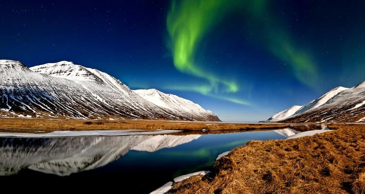 Green northern lights above snowy mountains and a river