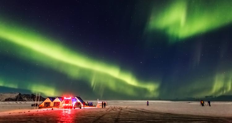 Green northern lights above a flat icy landscape and small buildings