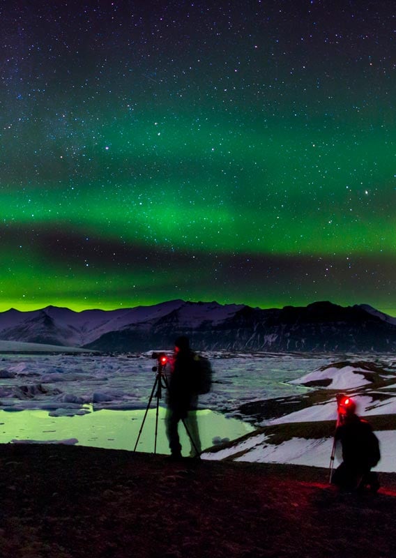 Two photographers set up their cameras under a night sky of green northern lights