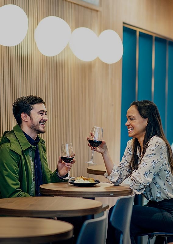 Two people sit at a cafe table with glasses of wine and dessert.