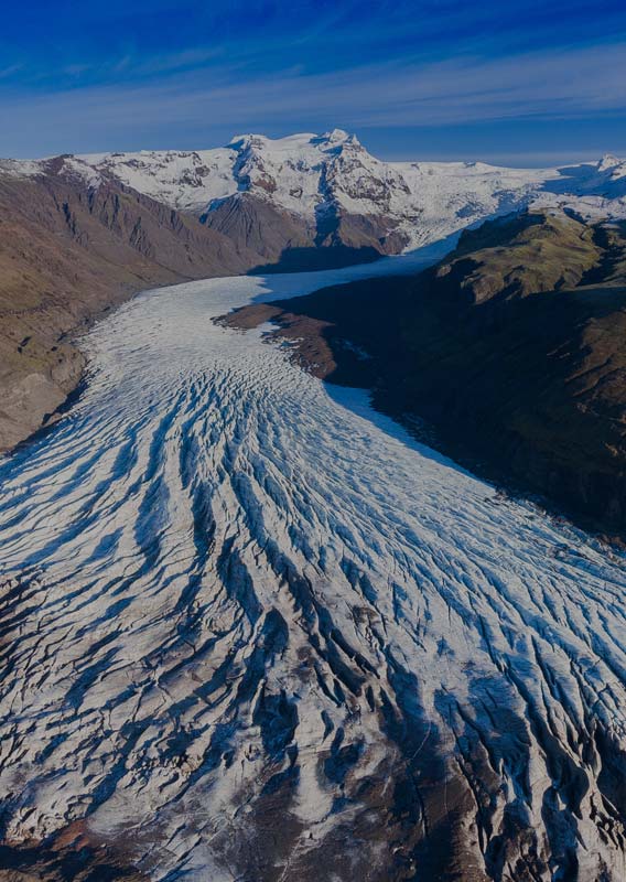 Stórir klakamolar fljóta um í lítilli vík um leið og sólin sest bak við snævi þakið fjall.