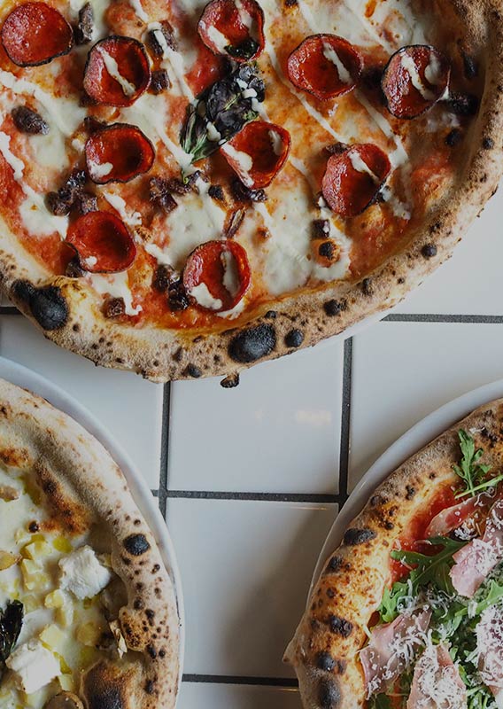 Four pizzas alternated on a white tile background
