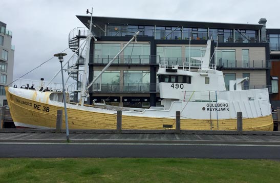 A yellow and white boat sat in a harbour next to a glass building