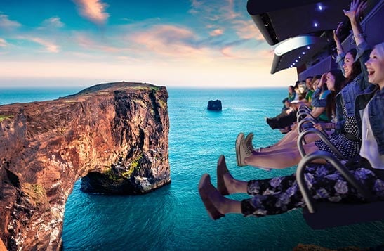 People on a flight ride superimposed over a scene of a rocky point at the sea.