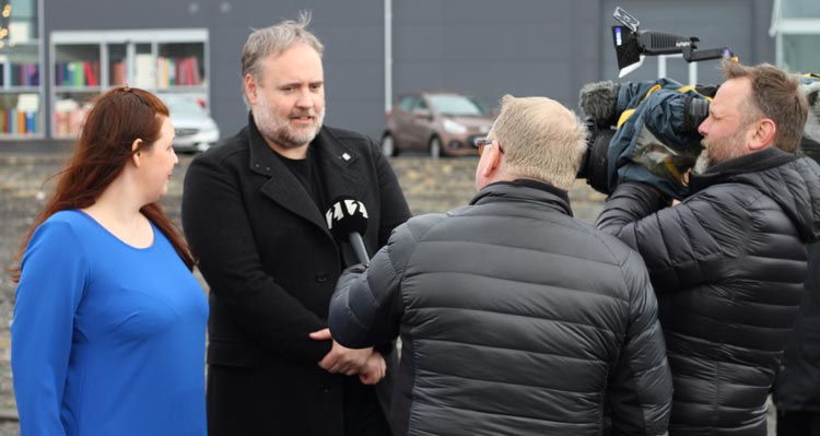 Sjónvarpsfréttamaður tekur viðtal við tvo menn við skóflustunguathöfn FlyOver Iceland.