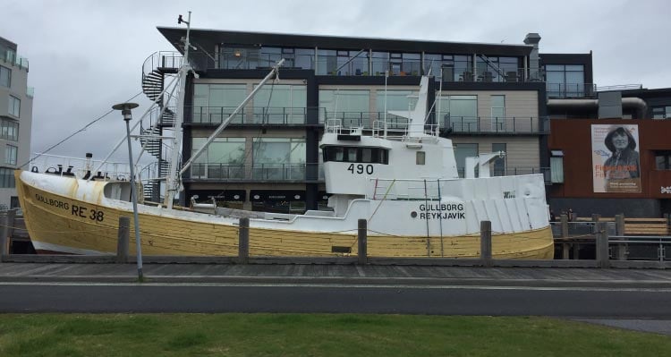 A yellow and white boat docked in front of modern buildings.