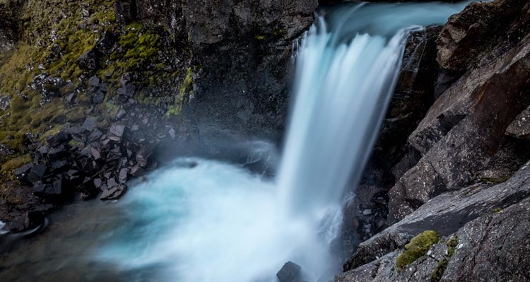 A blue waterfall crashes into a small pool of water.