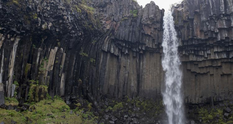A small waterfall falls between jagged rocks and moss.