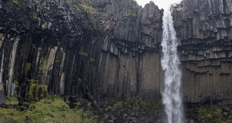 Lítill foss fellur á milli hvassra steina í mosa.