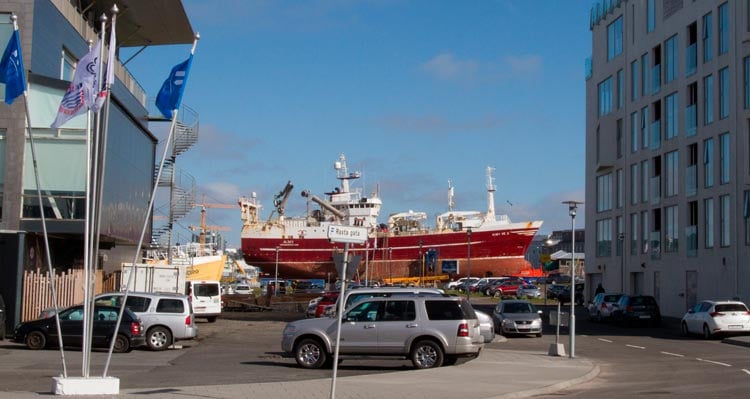 Bátur við festar í höfninni, með nýtískulegar byggingar í baksýn