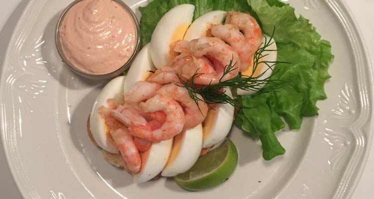 A plate of smørrebrød with prawns and hard-boiled egg and lettuce.
