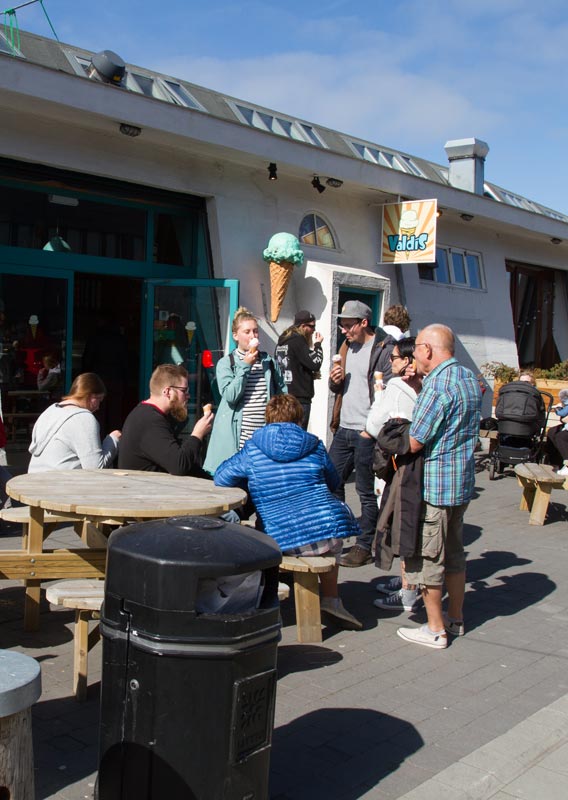 Crowds of people eat ice cream around wooden picnic tables on a sunny day.