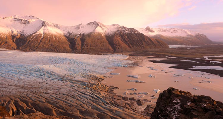 A glacier stretches below snow-capped mountains.