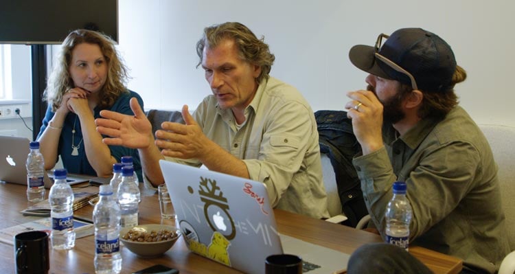 Three people sit at a desk, discussing a project.