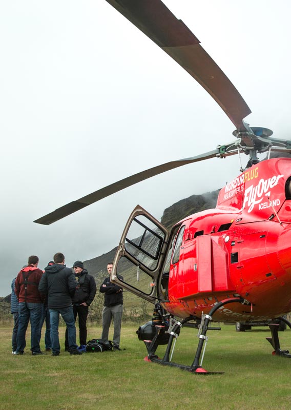 A film crew stands outside of a red helicopter under a low fog.