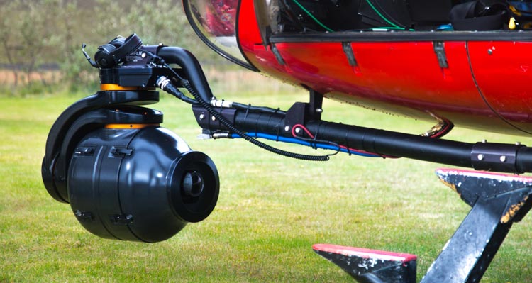 A close view of a camera attached to the underside of a red helicopter.