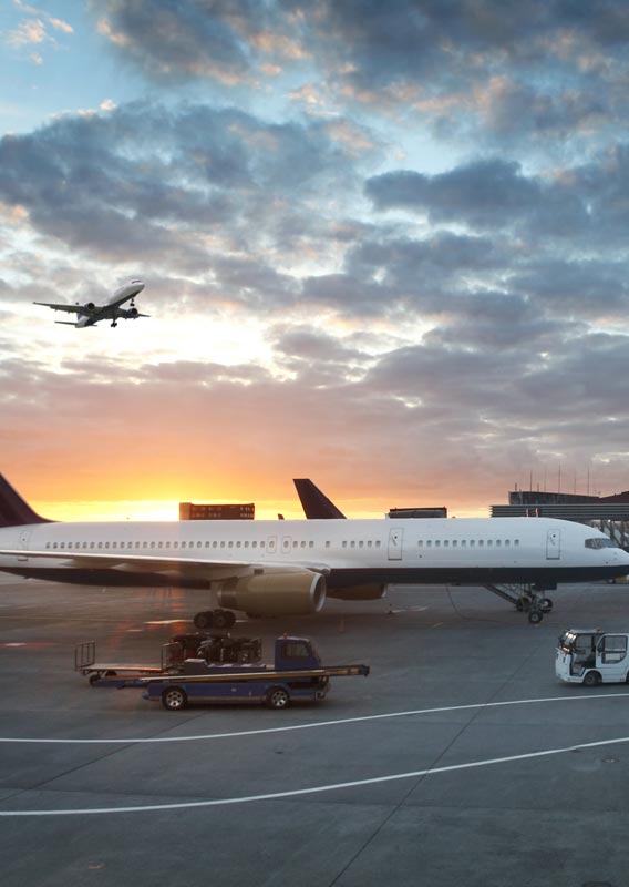 A plane parked at an airport as the sun sets behind.