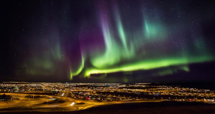 Græn og fjólublá Norðurljós skína yfir Reykjavík.