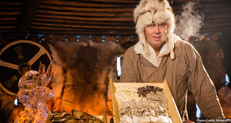 A man stands with food in a wooden house.