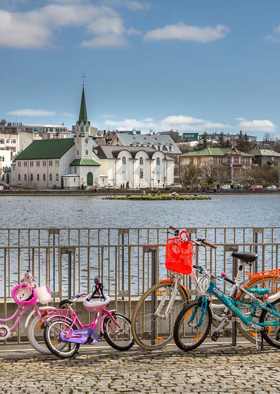 A view across a small lake towards a white church and other city buildings.