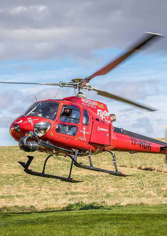 A red helicopter takes off from a grassy field.