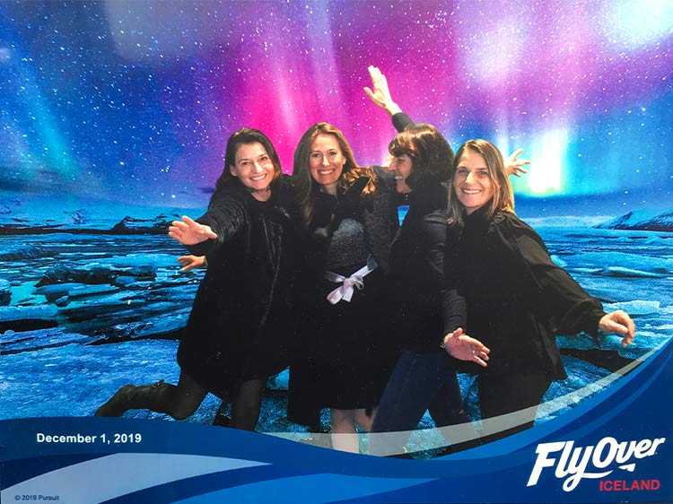 A group of people pose for a photo in front of a northern lights backdrop.