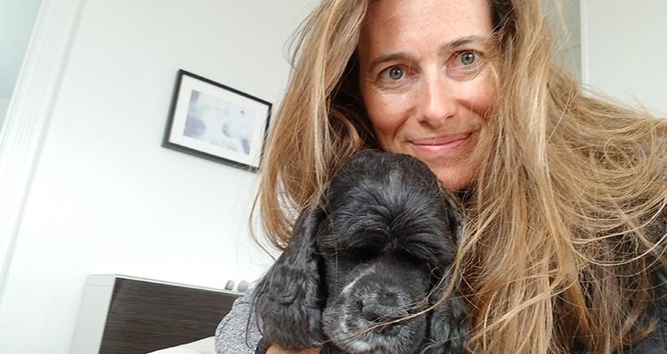 A woman holds a black dog close to her face.