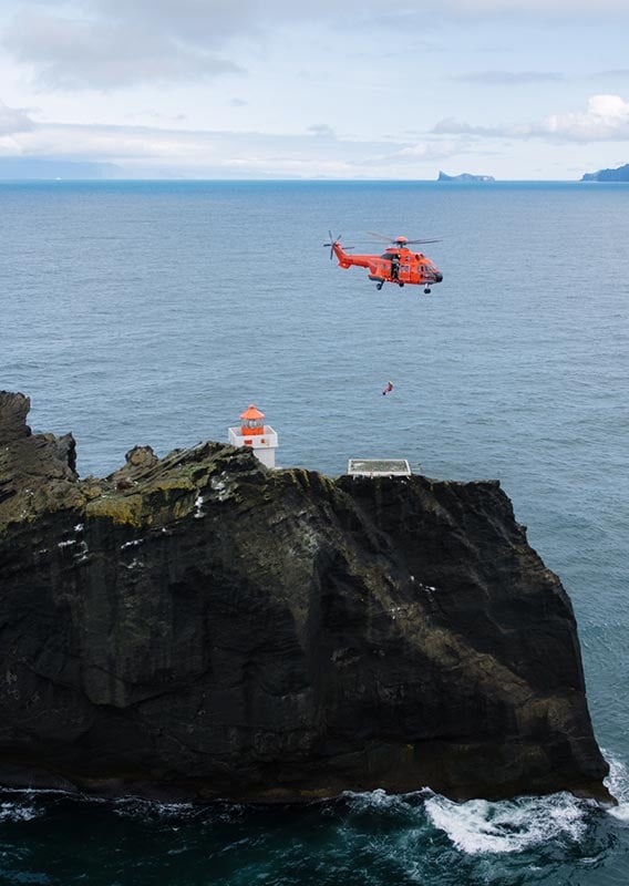 A helicopter hovers above a small island and lighthouse.