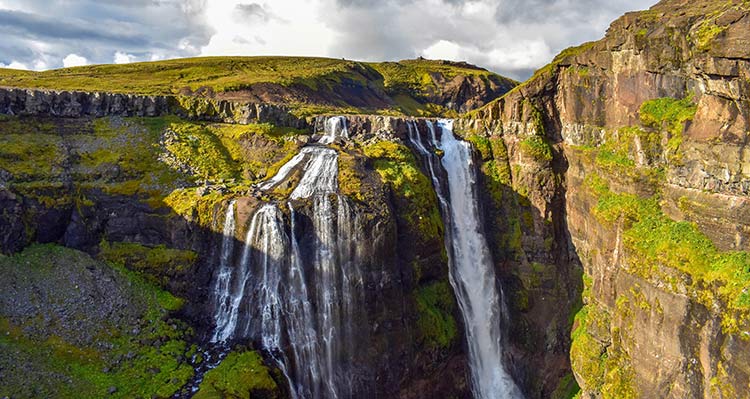 The waterfall Glymur. A tall waterfall rushes over mossy cliffs and smaller waterfalls flow alongside.