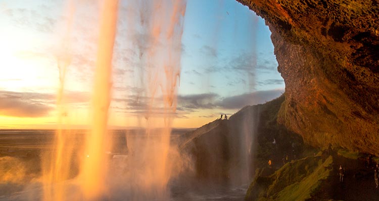 A view from behind a waterfall, Seljalandsfoss, coloured orange by sunlight.