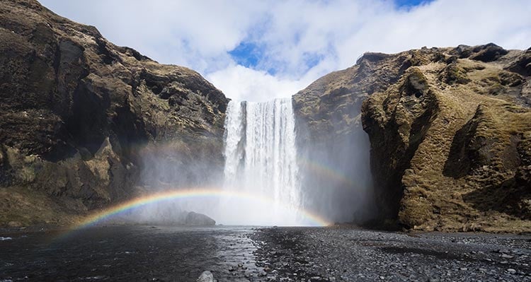 The waterfall Skogafoss. A tall waterfall crashes into a mist below tall cliffsides.