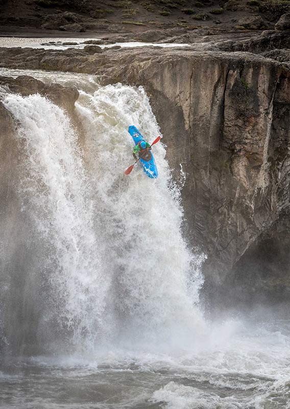 A kayaker descends down a waterfall into rushing water.