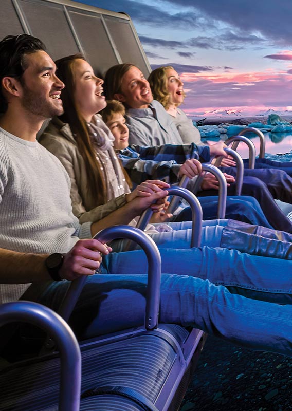 A group of people on the FlyOver Iceland flight ride with floating ice on the screen behind them.