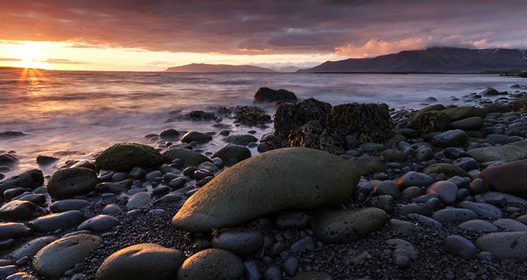 A close view of a rocky beach with the sun setting behind the sea.
