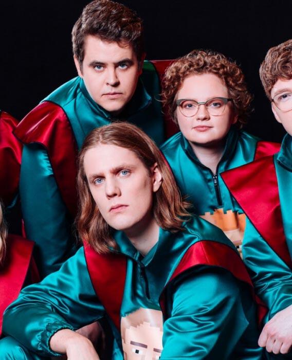 A group photo of people in a band, wearing shiny retro jumpsuits