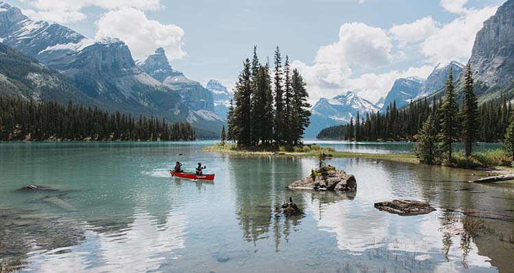 A red canoe floats near the shoreline of a mountain lake with trees in the background.