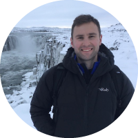 A man standing in a jacket in front of a snowy landscape.